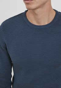 Mornarskoplavi pleteni pulover s horizontalnom rebrastom teksturom i okruglim izrezom, koji ističe glatki materijal s suptilnim detaljima.