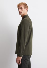 Olive green long-sleeve shirt with a collar, slim fit, buttoned cuffs, and smooth cotton fabric. Side view highlights design and fit.
