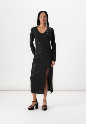 Black, long-sleeve dress with a v-neck and wave pattern, featuring a side slit. Paired with black block-heel sandals.