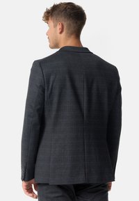 Schneiderblazer in Dunkelgrau mit einem subtilen Karomuster, strukturierten Schultern und matten Knöpfen. Glatte Textur mit modernem Schnitt.