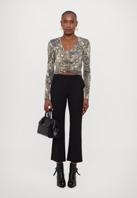 Top a maniche lunghe con stampa serpente in beige, nero e grigio, con scollatura a V profonda e dettagli arricciati. Abbinato a pantaloni neri attillati a vita alta e stivali alla caviglia.