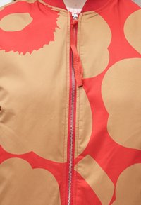 Czerwona i beżowa kurtka bomber z dużym abstrakcyjnym wzorem kwiatowym, centralnym zamkiem błyskawicznym i prążkowanym kołnierzem. Gładka faktura tkaniny.