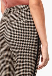 Pantalon à motif pied-de-poule en beige et noir, avec une coupe slim, des détails de rayures sur les côtés et une taille standard avec poches arrière.