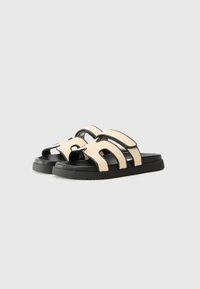 Dual-strap sandals featuring a beige fabric upper with black accents and a textured black rubber sole. Open toe design.