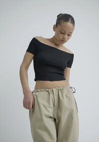 Crna krojena bluza s otkrivenim ramenima u kombinaciji s laganim bež hlačama. Bluza je priljubljena, a hlače imaju elastičan pojas s vezicama.