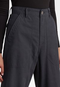 Mörkgrå byxor i ett strukturerat tyg, med hög midja, vida ben, snedställda framfickor och stängning med metallknapp.