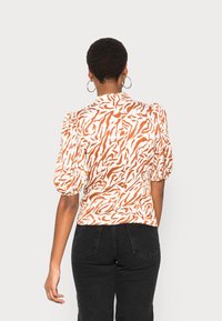 Blusa a maniche corte in stampa zebra arancione e bianca, con maniche a palloncino e colletto, realizzata in tessuto leggero.