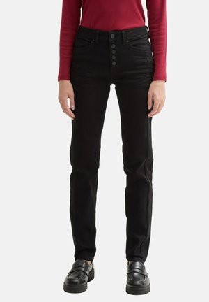 Jeans de mezclilla negra con un ajuste ceñido, cintura alta, cierre de cinco botones y bolsillos frontales. Llevados con una blusa roja de manga larga y zapatos negros.