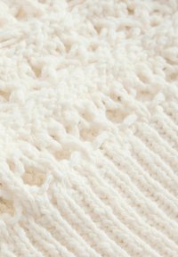 Tissu tricoté blanc présentant un motif texturé de boucles et de points, avec une apparence douce et épaisse et une couleur uniforme sur l'ensemble.