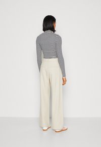 Pasiasty dół z długim rękawem w czerni i bieli, w zestawieniu z kremowymi spodniami z szerokimi nogawkami. Obuwie ma białą bazę z różowymi i pomarańczowymi paskami.