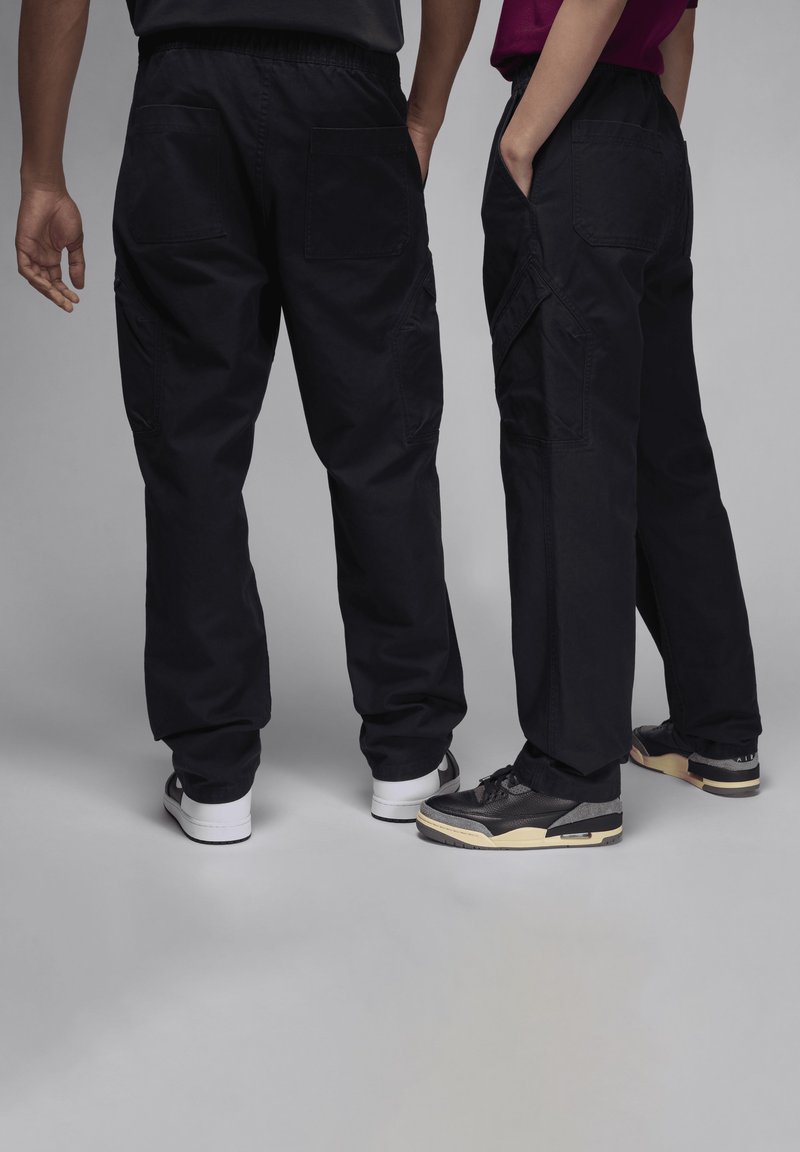 Pantalones cargo negros con bolsillos laterales, cinturillas elásticas y un ajuste relajado. Dos pares de zapatillas en colores contrastantes complementan el look.