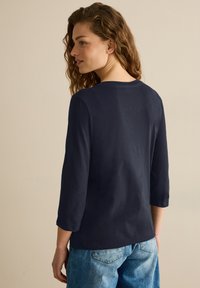 Mörkblå, långärmad topp med rundad halsringning och avslappnad passform, tillverkad av mjukt tyg. Kombinerad med ljusblå denimjeans.