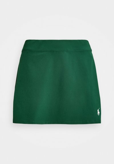 Zelená sukňa vyrobená z hladkej tkaniny. Má rovný strih, široký pás a malé biele logo na dolnej pravej strane.