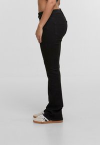 Pantalones de mezclilla negros con un corte recto, que cuentan con una cintura de altura media, bolsillos traseros y una textura suave, combinados con zapatillas deportivas blancas.