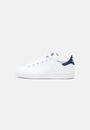 Sneaker bianche in pelle con texture liscia, caratterizzate da dettagli blu navy sul tallone e sulla linguetta, progettate con strisce perforate sui lati.
