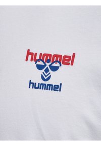 Hvidt stof med rød "hummel"-tekst over en blå bi-logo og blå "hummel"-tekst nedenunder, centreret på stofoverfladen.