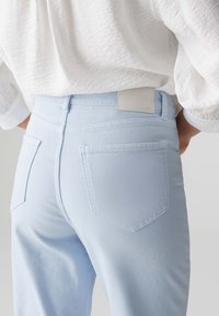 Jeans en denim bleu clair avec une taille haute, deux poches arrière et des détails de couture minimaux. Le matériau semble doux avec une légère élasticité.