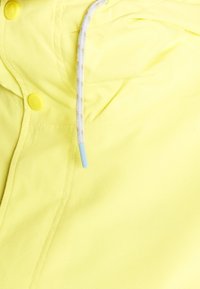 Gul vattentät jacka med dragstring i huvan med blåa spetsar och gula tryckknappar på framsidan. Slät textur.