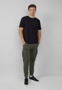 Zwarte T-shirt met korte mouwen en textuur, gecombineerd met olijfgroene cargo broek met zijzakken, gedragen met zwarte sneakers met witte zolen.