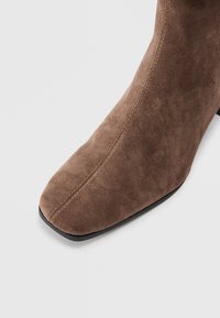 Brun mocka ankelsko med fyrkantig tå och slät yta. Har en elegant design och en hållbar svart sula.