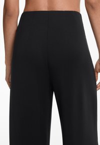 Pantalons larges noirs en tissu lisse, avec une taille haute, des coutures à l'arrière, et sans poches ni ornements visibles.