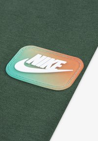 Tissu vert avec une finition texturée, présentant une patch en caoutchouc dégradé affichant le logo Nike en blanc.
