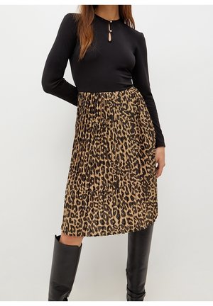Woman wearing black long-sleeve top with keyhole neckline, leopard-print pleated midi skirt, and black knee-high boots against white background.