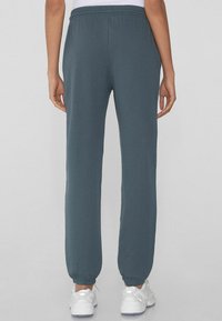 Dunkelgrüne Sweatpants mit elastischem Bund und Bündchen an den Knöcheln, die eine glatte Textur und einen bequemen, lockeren Schnitt bieten.