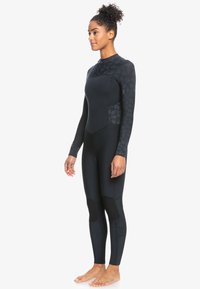 Traje de neopreno negro con mangas largas y cuello alto. Presenta paneles texturizados y con diseño en los brazos y áreas de rodillas reforzadas. Material elástico diseñado para deportes acuáticos.