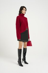 Rdeča, oversize turtleneck pulover, v kombinaciji z črno mini krilo z značilnimi srebrnimi studenčki. Črne, visoke, lakirane čevlje z visokimi petami in mala rdeča torbica.
