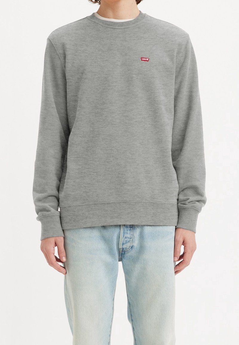 Sudadera gris de mezcla de algodón suave con puños y dobladillo acanalados. Presenta un pequeño logotipo rojo de Levi's en el pecho. Combinada con jeans de color azul claro.