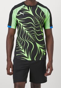 Svart träningsskjorta med grönt bladmönster, meshärmar och blå trim. Tillverkad av fukttransporterande material för aktiv användning.