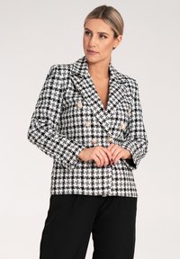 Dwurzędowa marynarka w czarno-białą kratę, z metalowymi guzikami i teksturowanym materiałem. Dopasowany krój, klapy z wycięciem.