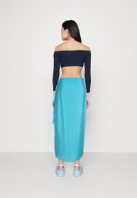 Modra satenska krila z zavojem, v kombinaciji z mornarsko modrim, off-shoulder crop topom. Gladka tekstura, dolžina do tal in odprt hrbet.