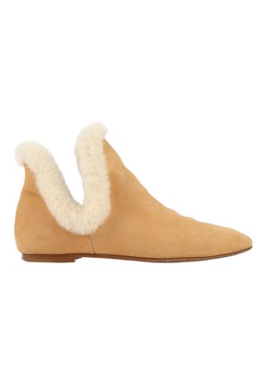 Chaussure plate en daim beige avec un bout pointu et une bordure en shearling duveteuse crème autour de l'ouverture de la cheville, vue latérale sur fond blanc.