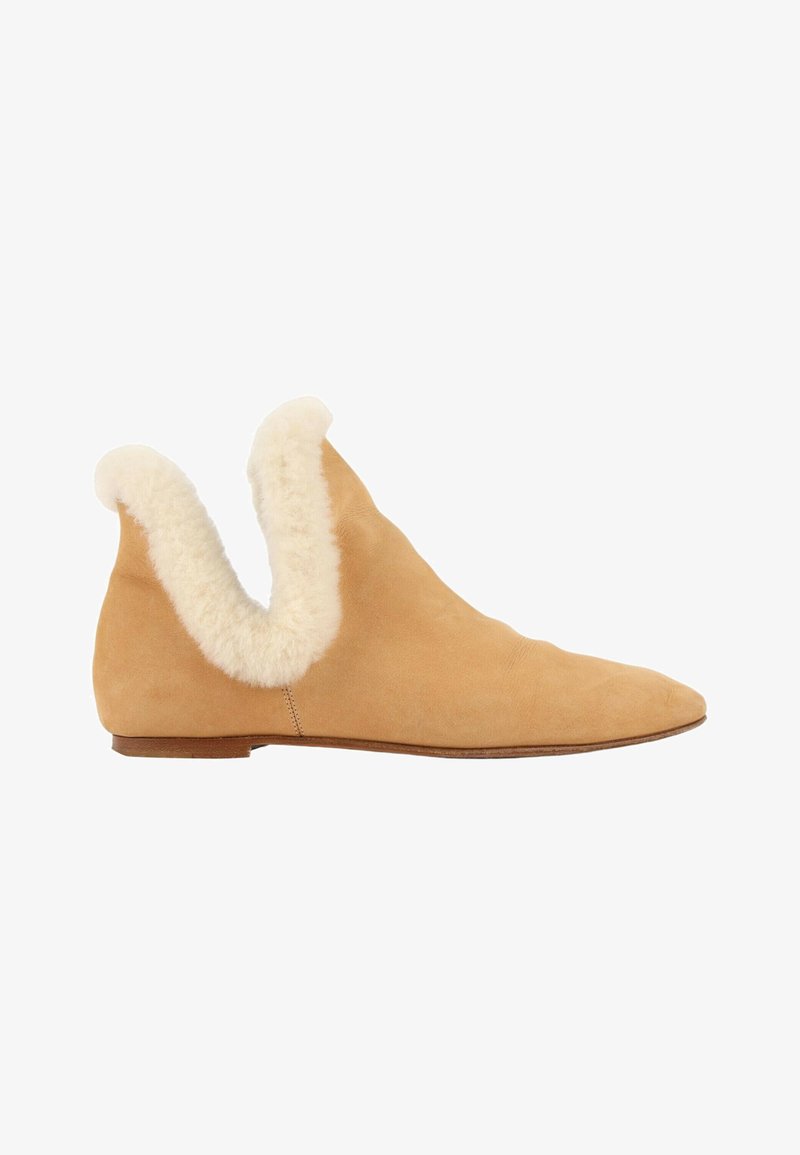 Chaussure plate en daim beige avec un bout pointu et une bordure en shearling duveteuse crème autour de l'ouverture de la cheville, vue latérale sur fond blanc.