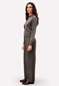 Pull en maille gris avec un col et un détail de boutons, associé à un pantalon large gris assorti et des chaussures en cuir marron, vu de profil.