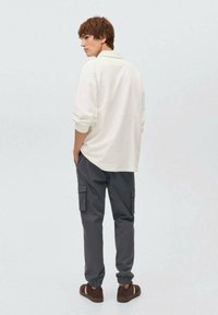 Valkoinen pitkähihainen paita, jossa on pudotetut olkapäät, yhdistettynä tummanharmaisiin cargo-housuihin, joissa on sivutaskut ja elastiset hihan suut. Ruskeat kengät.