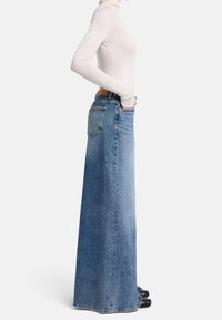 Pitkä sininen farkkuhame, korkea vyötärö ja suora leikkaus. Varustettu takataskulla ja hienovaraisella haalistumisella. Yhdistetty tiukasti istuvan valkoisen kauluspuseron kanssa.