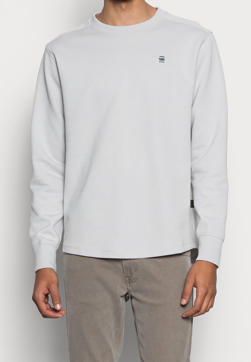 Sweatshirt gris clair à manches longues avec col rond, coupe décontractée, détail de logo subtil sur la poitrine, fabriqué en tissu de coton doux.