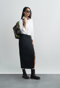 Czarna spódnica midi z bocznym zamkiem, zestawiona z białą koszulą z kołnierzykiem. Modelka nosi czarne botki oraz ma na plecach plecak w kwiatowy wzór.