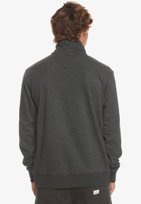 Felpa lunga grigia scura con maniche lunghe e colletto alto, polsini e orlo a costine. Tessuto morbido, design minimalista, senza motivi o loghi visibili.