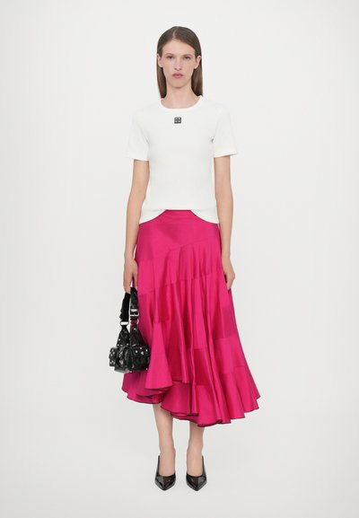 Haut blanc à manches courtes avec un logo, associé à une jupe en satin fuchsia à couches. Le modèle tient un petit sac à main noir et porte des talons aiguilles noirs.