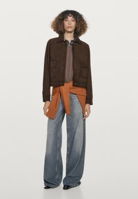 Bruine suède cropped jas, oversized lichtblauwe spijkerbroek, roestrode trui gestrikt in de taille, gladde textuur, ontspannen ontwerp.