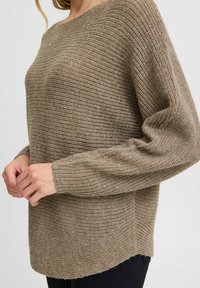 Beiger, gestrickter Pullover mit strukturiertem Muster, lockerer Passform und weiten Ärmeln. Der Saum ist hinten etwas länger.