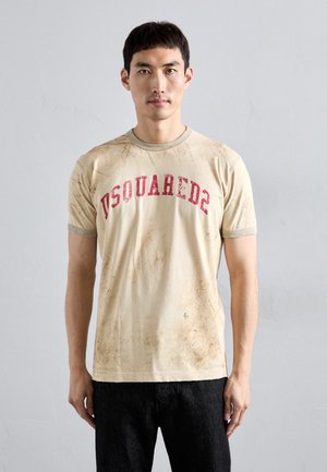 Beige Baumwoll-T-Shirt mit rotem "DSQUARED2"-Druck, kurzen Ärmeln und einem abgenutzten Textur. Kombiniert mit dunklen Jeans.