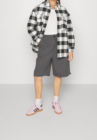 Plaid black and white flannel shirt over a white tank top, paired with gray shorts and pink sneakers with dark accents. Textured fabric details visible.