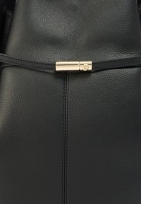 Μαύρη δερμάτινη τσάντα με ομαλή υφή, που διαθέτει χρυσό μεταλλικό κούμπωμα και διακριτικές ραφές κατά μήκος του κέντρου.