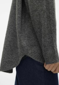 Szary wełniany sweter o teksturowanym wykończeniu, z asymetrycznym dołem i ściągaczami na rękawach. Kompletnie zestawiony z ciemnoniebieskim dżinsem.