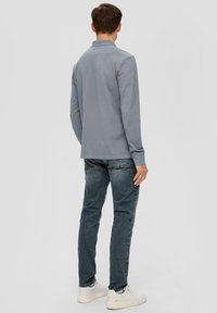 Graues langärmliges Polohemd mit Kragen, getragen mit blauen Jeans und weißen Sneakers. Glatte Textur und lässiger Schnitt.